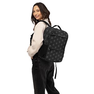May include: Black backpack featuring a white geometric design. It has a top handle, side pocket, and adjustable straps. The backpack is worn over the shoulders.
