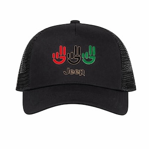 Puede incluir: Gorra de camionero negra con parte trasera de malla y visera curva. La parte delantera presenta tres gestos de manos en rojo, negro y verde, con la palabra "Jeep" debajo. Un accesorio clásico.