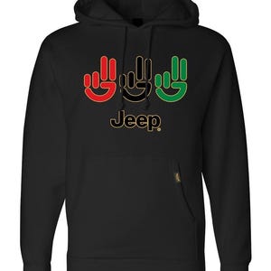 Puede incluir: Sudadera con capucha negra con un diseño de símbolo de mano rojo, negro y verde y la palabra "Jeep" en letras doradas.