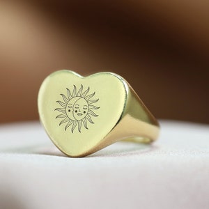 May include: A gold heart-shaped signet ring with a sun and moon design engraved on the face.