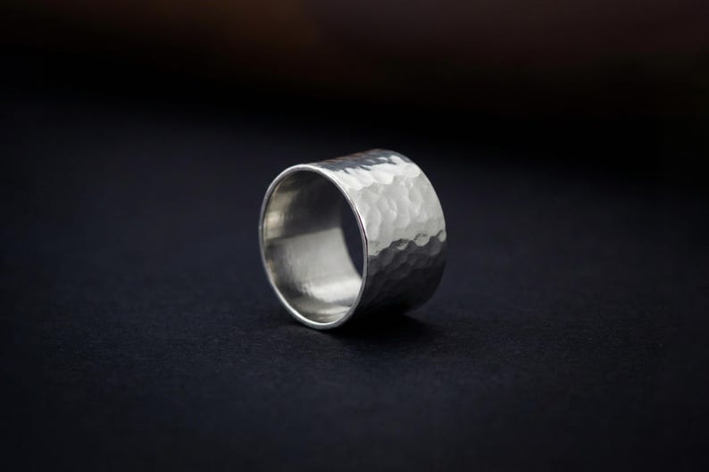A silver ring with a textured surface sits on a dark background.