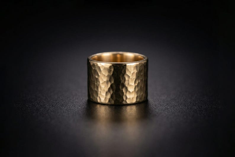 A shiny gold ring with a textured surface sits on a dark surface, creating a striking contrast.