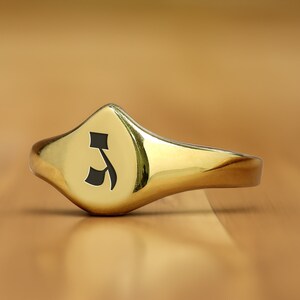 May include: A gold signet ring with a black Hebrew letter 'aleph' engraved on the face.
