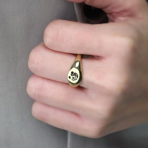 May include: A gold signet ring with a black and white panda design.