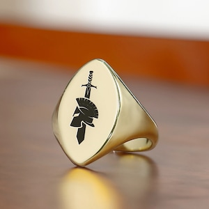 May include: A gold signet ring with a black and white image of a Roman helmet and sword.