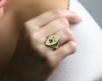 Può includere: Un anello a sigillo in oro con un designo in bianco e nero di una creatura che indossa una corona.