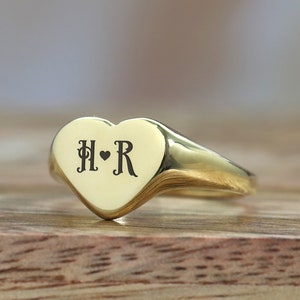 May include: A gold heart-shaped ring with the initials "H" and "R" engraved on it, separated by a small heart.