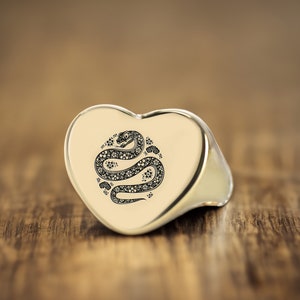 May include: A silver heart-shaped ring with a black and white snake design.