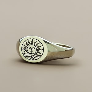 May include: A silver signet ring with a sun and waves design. The sun has a face and is surrounded by rays. The waves are below the sun.