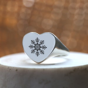 May include: A silver heart-shaped ring with a snowflake design engraved on the top.