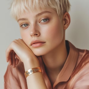 May include: A person wearing a gold bracelet with the inscription "You Are Loved".