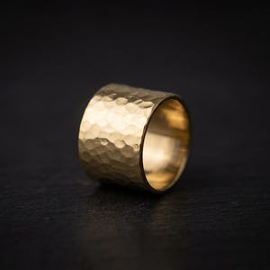 A shiny gold ring with a textured surface sits on a dark surface, creating a striking contrast.