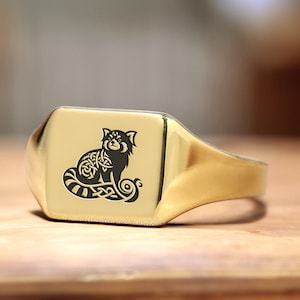 May include: A gold signet ring with a black and white engraved image of a red panda with a Celtic knot design.