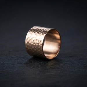 A close-up image of a gold ring with a textured surface, resting on a dark surface.