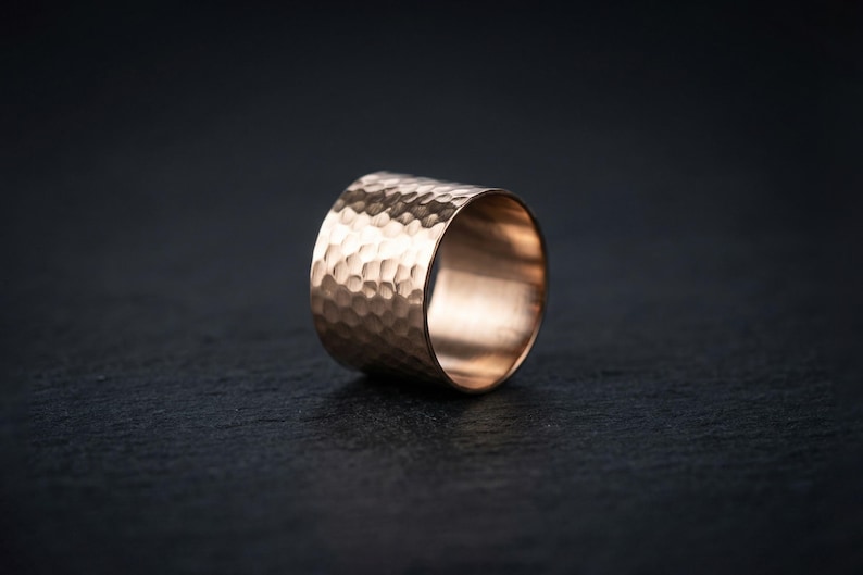 A close-up image of a gold ring with a textured surface, resting on a dark surface.