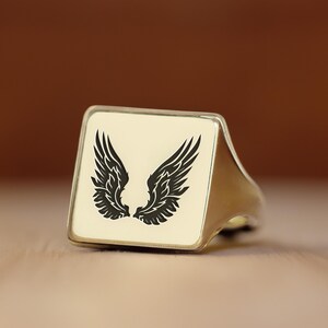 May include: A gold ring with a square black and white design of angel wings.