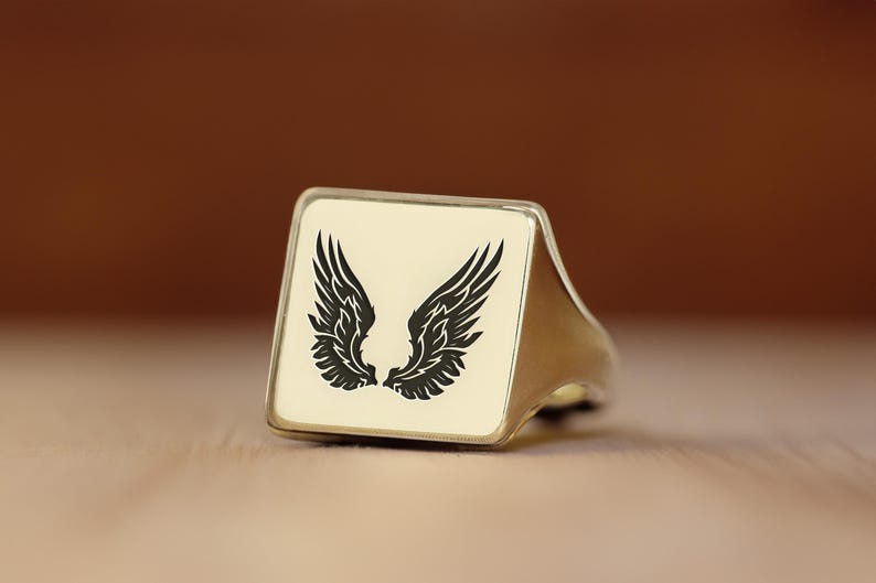 May include: A gold ring with a square black and white design of angel wings.