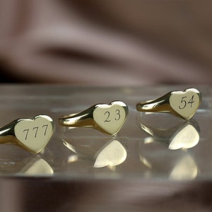 以下が含まれることがあります： 数字が刻まれた金色のハート型の指輪が3つあります。指輪は777、23、54です。