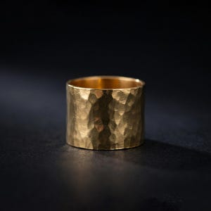 A shiny gold ring with a textured surface sits on a dark surface, casting a shadow.