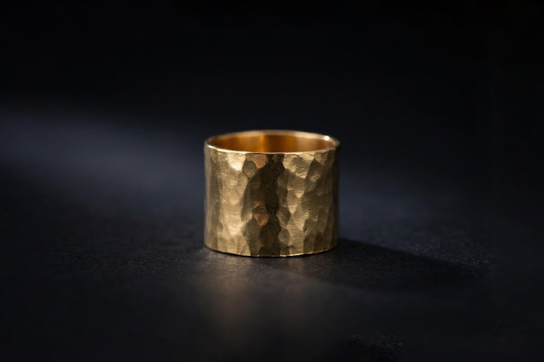 A shiny gold ring with a textured surface sits on a dark surface, casting a shadow.