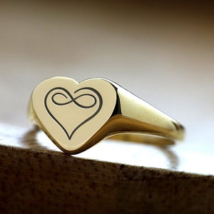 May include: A gold heart-shaped signet ring with an infinity symbol engraved inside the heart.