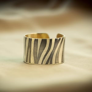 May include: A gold and black patterned metal ring with a zebra-like design.