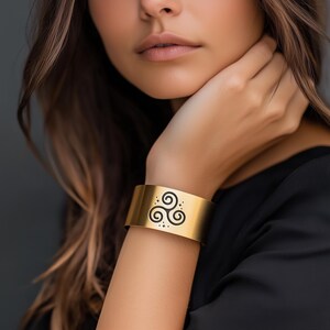 May include: A gold cuff bracelet with a black Celtic knot design. The bracelet is wide and has a smooth, polished finish.