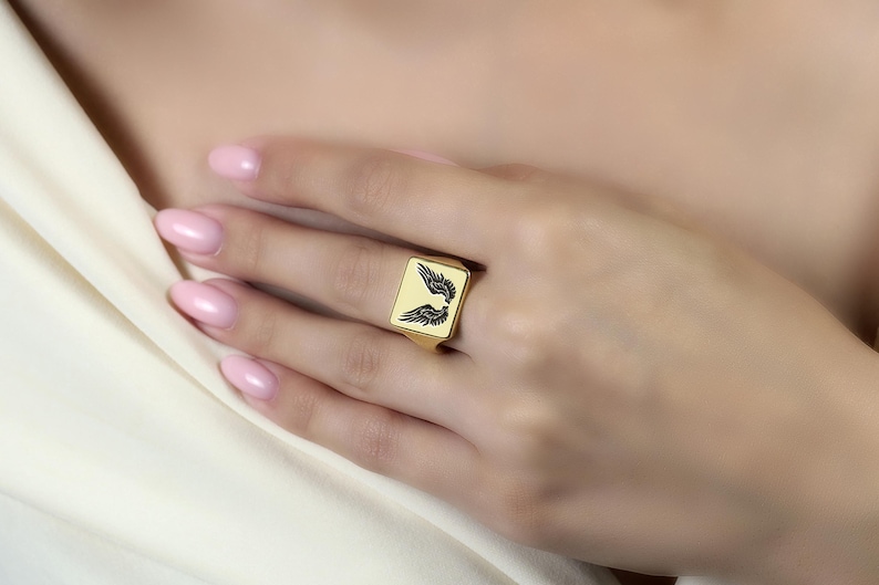 May include: A gold signet ring with a black wing design.