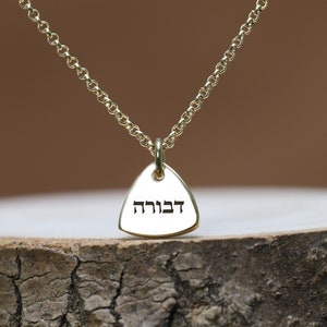 May include: Gold necklace with a triangular pendant inscribed with the Hebrew word "דברוה" (Devorah).