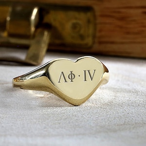 May include: A gold heart-shaped signet ring with the inscription "ΛΦ·IV".