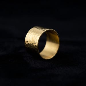 A shiny gold ring with a textured surface is displayed against a dark background.