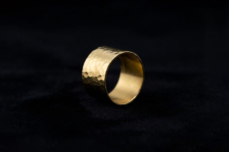 A shiny gold ring with a textured surface is displayed against a dark background.