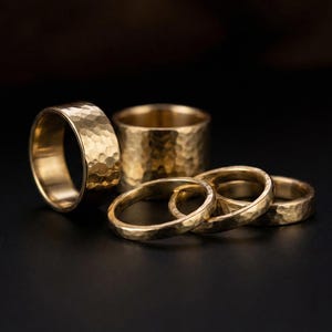 A collection of gold-colored rings with a textured, embossed appearance, arranged on a dark background.