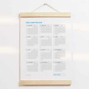 May include: A 2026 Camp Tracker calendar with a wooden frame. The calendar features a grid layout with circles for each day of the month. The text "2026 CAMP TRACKER" is at the top. The calendar is designed to track camp activities.