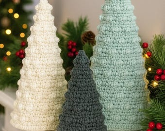 Könnte beinhalten: Drei gehäkelte Weihnachtsbäume in verschiedenen Größen und Farben. Die Bäume sind weiß, grau und hellblau. Die Bäume werden auf einer weißen Oberfläche mit weihnachtlichem Grün im Hintergrund ausgestellt.