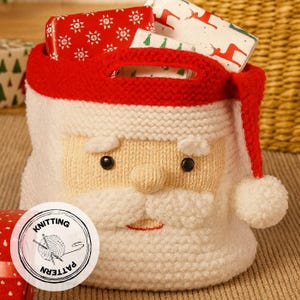 Op de afbeelding: Een gebreide tas in de vorm van de Kerstman met een rode hoed en handvat, gevuld met ingepakte cadeaus. De tas heeft een witte gezicht met een beige neus en zwarte ogen. Een sticker "Knitting Pattern" staat op de voorkant.