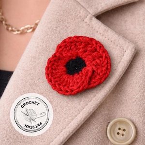 May include: A handmade red crochet poppy flower with a black center, pinned to a beige coat. The poppy is a symbol of remembrance. A round sticker with the words "CROCHET PATTERN" surrounds a yarn ball and crochet needles.