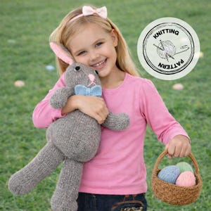 May include: A girl smiles, holding a grey knitted bunny with pink ears and a blue bow tie. She also holds a small woven basket with three colourful knitted eggs. A pink bow headband and a pink long-sleeved top are also visible. The image includes a 'Knitting Pattern' logo.
