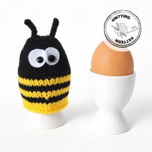 Op de afbeelding: Een gebreide bijen-eierwarmer met zwarte en gele strepen, grote witte ogen en zwarte antennes, naast een bruin ei in een witte eierdop. De afbeelding bevat een cirkelvormig logo met de tekst "Knitting Pattern".
