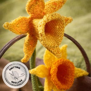 May include: Two knitted daffodil flowers in yellow and orange hues. The flowers are crafted with textured yarn, highlighting the detailed knitting pattern. A circular logo with the words "Knitting Pattern" is visible, suggesting a craft project.