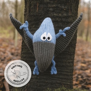May include: A knitted pterodactyl toy in blue and grey, with large white eyes. The toy is attached to a tree trunk. A circular label with the words "Knitting Pattern" and a yarn ball is visible.