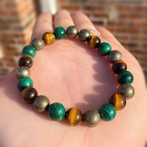 May include: A bracelet made with brown tiger's eye, green malachite, and gold pyrite beads.