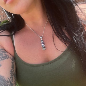 May include: A silver chain necklace with a pendant featuring five round, iridescent stones in shades of purple, blue, and green.