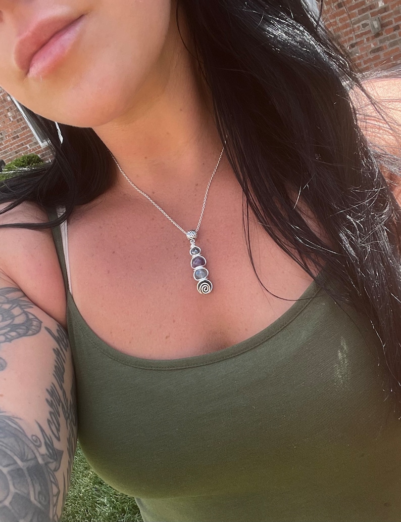 May include: A silver chain necklace with a pendant featuring five round, iridescent stones in shades of purple, blue, and green.