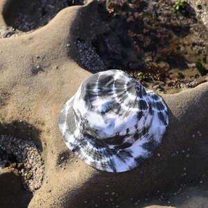 May include: A black and white tie-dye bucket hat on a sandy beach.