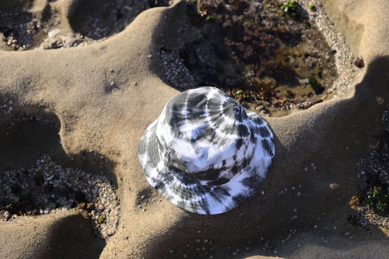May include: A black and white tie-dye bucket hat on a sandy beach.
