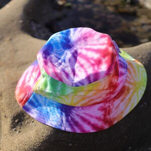 May include: A colorful tie-dye bucket hat with a rainbow pattern. The hat is made of a soft, lightweight fabric and has a wide brim.
