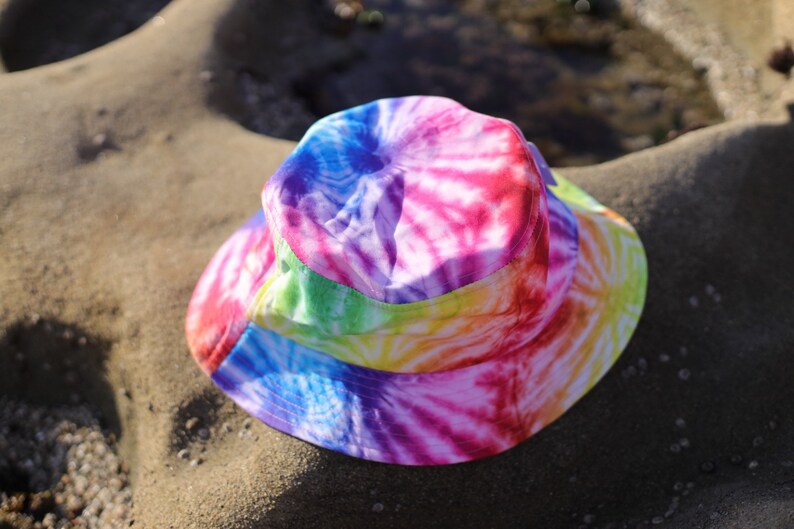 May include: A colorful tie-dye bucket hat with a rainbow pattern. The hat is made of a soft, lightweight fabric and has a wide brim.