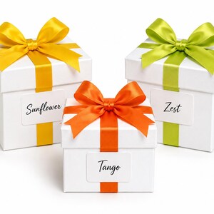 May include: Three white gift boxes with colorful bows and ribbons. The boxes are labeled "Sunflower", "Tango", and "Zest". The bows are yellow, orange, and green. The ribbons match the bow colors.