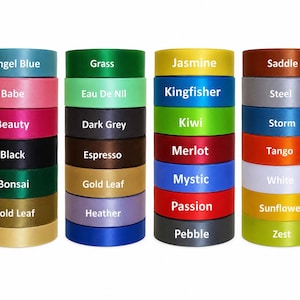 May include: A collection of satin ribbon rolls in a variety of colours, including blue, pink, green, and yellow. Each roll is labelled with its colour name, such as "Angel Blue," "Babe," and "Jasmine." The ribbons are neatly stacked, displaying a wide spectrum of shades.